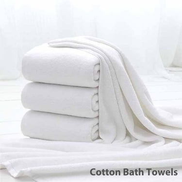 a stack of Cotton Bath towels and towels on a bed