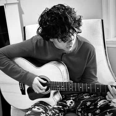 a man playing guitar in a chair black and white