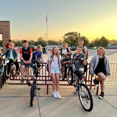 Group of kids on bikes parked at a bike rack posing for the camera