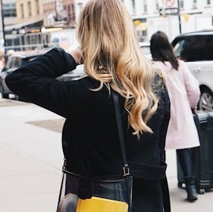 A woman with long blonde hair wearing a black coat walking outside