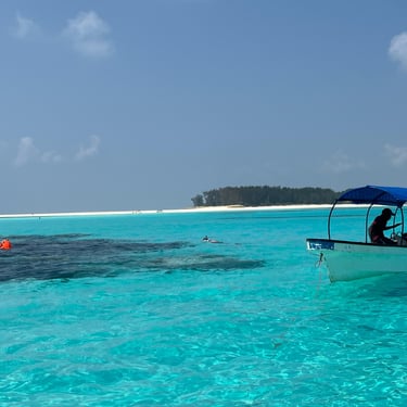 Tourists snorkeling near a boat anchored in shallow turquoise waters at Mnemba Island Zanzibar during a tropical snorkeling 