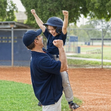 A parent-coach lifts a his player to celebrate on the baseball field.