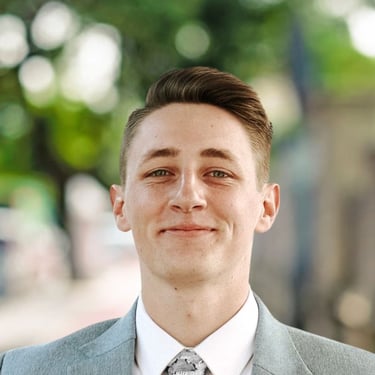 Portrait of Parker Oelrich, smiling slightly while wearing a light gray suit jacket, white shirt, an