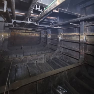 Internal view of a dark industrial steel ship hull cargo hold with metal pipes and structural ribs
