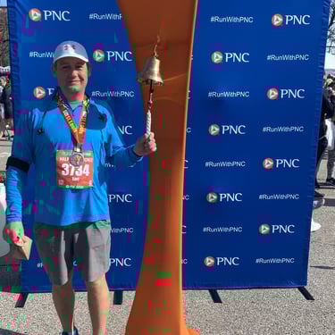 Man wearing a metal and running number, ringing a bell, posing for the camera