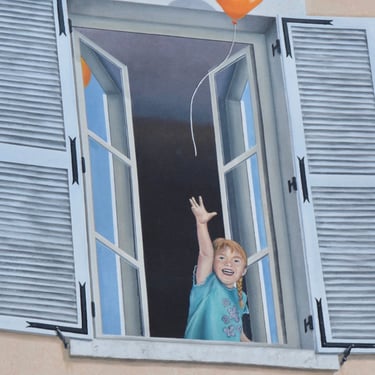 Détail d'un trompe-l'oeil sur façade à Moirans-en-Montagne: Une fillette à une fenêtre au 1er étage.