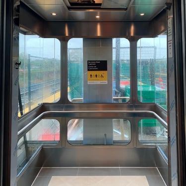 glass elevator showing outside, with a stainless handrail, tile floor and stainless ceiling