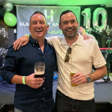 Two men standing together at a community event, holding drinks and smiling