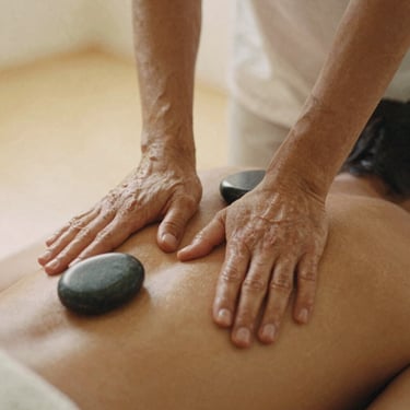 Hands applying pressure to a back during a deep tissue massage, smooth basalt stones nearby, soft diffused golden-hour light, earthy muted tones, shallow depth of field, 35mm film