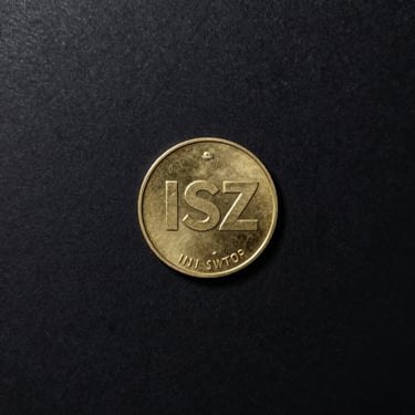 Overhead flat-lay on a near-black surface, a single gold ISZ token coin in sharp isolation at center frame, studio strobe lighting casting a hard rim of gold light around the coin's edge, minimal shadow underneath, clean dark background with no surrounding clutter