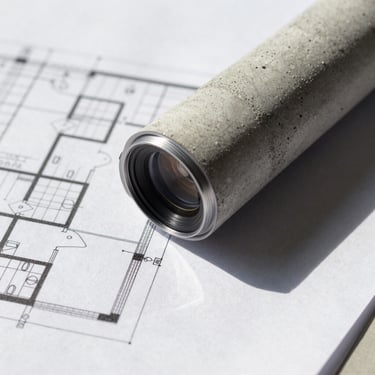 Close-up of a physical architectural blueprint and concrete texture under natural daylight, sharp shadows, minimal aesthetic.