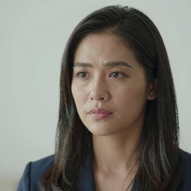A professional Asian woman with long dark hair looking thoughtful in a corporate office setting.