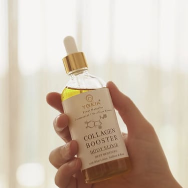 Hand holding a bottle of Ygeia Collagen Booster Body Elixir with a glass dropper in soft natural light.