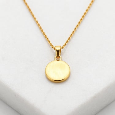 Crisp macro shot of a delicate gold pendant necklace resting on a white marble pedestal, soft golden reflections