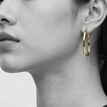 Macro portrait of a model wearing minimalist gold hoop earrings, high-key studio lighting