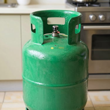 Close-up of a vibrant green cooking gas cylinder, brand new, sealed with a safety seal, bright daylight, authentic kitchen setting