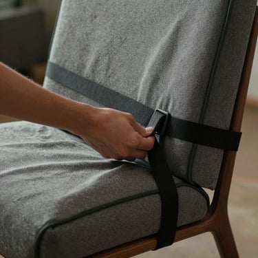 Close-up of a hand adjusting a thick, heavy-duty protective textile blanket wrapped around a mid-century modern chair, secured with a black utility strap.