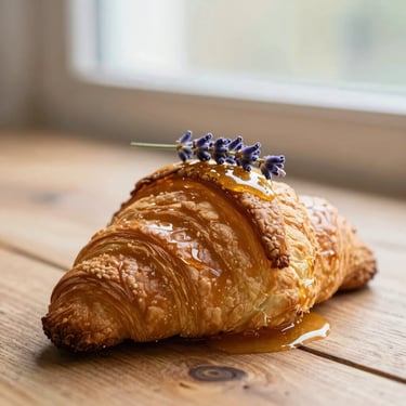 A golden, flaky croissant topped with a delicate sprig of fresh lavender and a drizzle of honey.