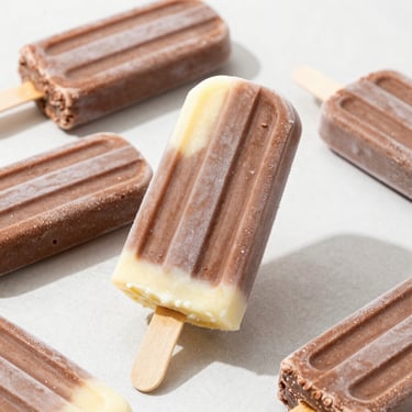 Vibrant eye-level shot of creamy chocolate and vanilla ice cream popsicles on a clean light surface, rich texture, crisp details.