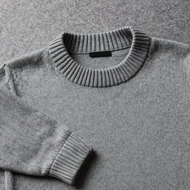 Flat lay of a heavy-weight cotton crewneck sweater in stone gray, highlighting the tight knit and thick collar ribbing.