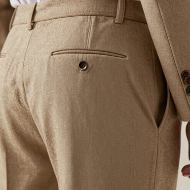 Close-up of tailored trousers in sand-colored linen, showing the clean drape of the fabric and precise pocket stitching.