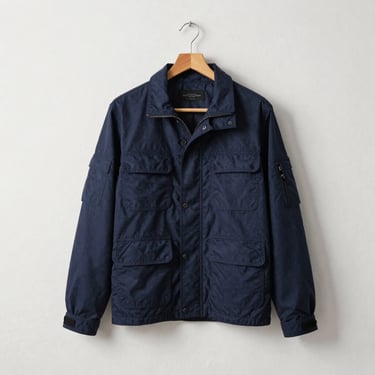 Unstructured utility jacket in deep navy canvas draped on a wooden hanger against a clean plaster wall.