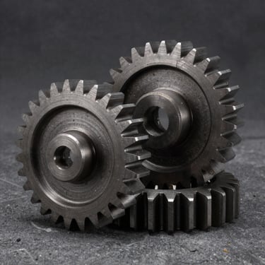 Macro studio shot of heavy-duty steel gears with metallic highlights, dark concrete background, industrial product photography