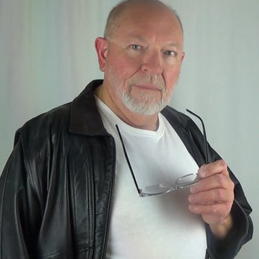 David-Graham Parker wearing a white T shirt a black leather jacket holding his glasses