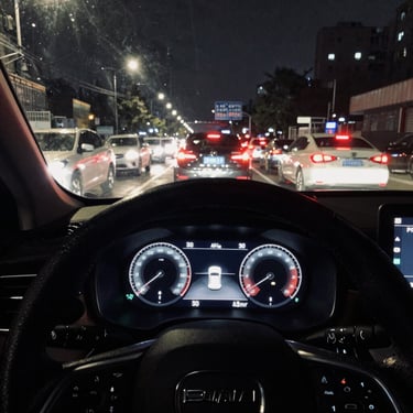 A premium vehicle dashboard displaying active ADAS telemetry overlays, navigating dense urban traffic at night with sharp headlight glare, desaturated industrial tones.