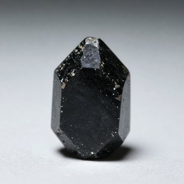 Extreme close-up of a single raw black tourmaline specimen on a plain pale surface, north-facing daylight, no props, 1:1 scale