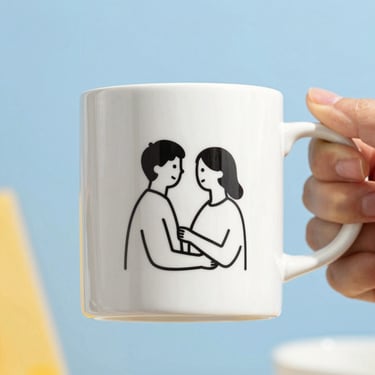 Close-up of a white ceramic mug with a clean black line-art drawing of the same couple, held by hands, sky blue background