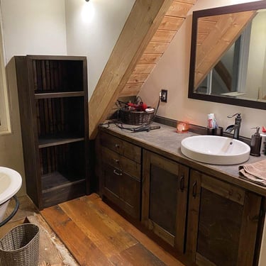 Rustic bathroom interior with a dark wood vanity, vessel sink, wall mirror, shelving, and warm lighting.