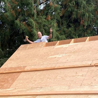 Worker with a power drill behind a roof frame under construction.