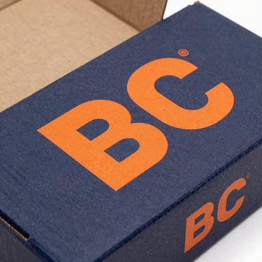 Flat-lay of an unfolded printed corrugated box with high-contrast industrial orange branding, clean studio lighting