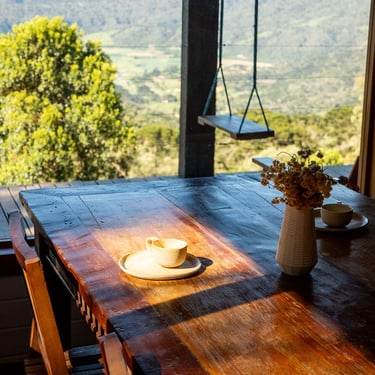 Mesa de jantar da cabana Wolken Haus Urubici com uma xícara de café e flores e ao fundo a vista panorâmica das montanhas