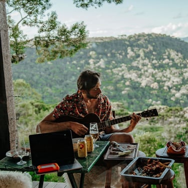 Hospede toca violão e mesa de churrasco na varanda da cabana com vista panoramica e montanhas ao fundo