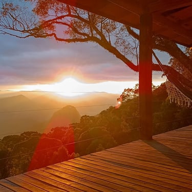 Varanda da cabana Wolken Haus Urubici com uma rede e vista panoramica das montanhas com o sol nascendo ao fundo