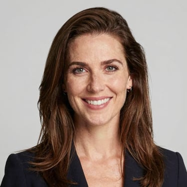 A smiling woman with curly hair enjoying a sunny outdoor cafe.