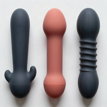 Overhead studio shot of three special-form silicone dildos on a white surface arranged in a precise row — one double-ended, one curved, one with textured ridges. Strong overhead studio lighting reveals surface detail and material differences. No props.