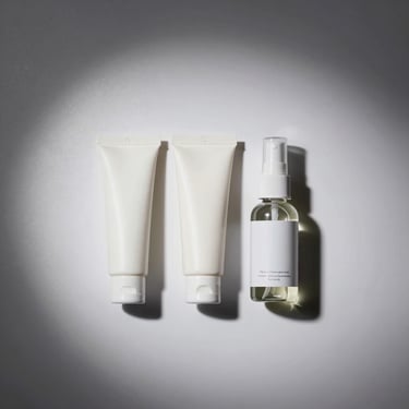 Overhead studio shot of three small product tubes and a spray bottle of intimate stimulating gel arranged in a clean row on white surface, strong overhead directional light showing label-free packaging and material texture, grey background, no people