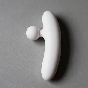 Close-up overhead studio shot of a wand massager vibrator in white ABS silicone on grey surface, strong side light revealing rounded head and textured grip, no people