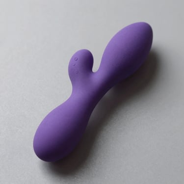 Studio shot from above of a rabbit vibrator in purple silicone on grey surface, side lighting revealing dual-arm structure and texture, no lifestyle elements