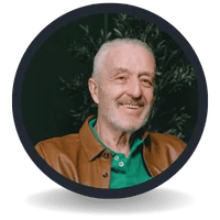 Smiling senior man with a beard wearing a brown leather jacket and green shirt in a circular portrait.