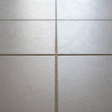 Extreme close-up of freshly laid ceramic floor tiles in a Seville apartment, tight grout lines perfectly aligned, natural overcast daylight raking across the surface revealing texture, no people