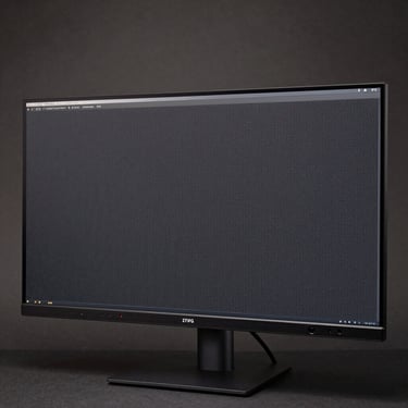 Overhead close-up of a 27-inch IPS monitor face-on on a neutral dark surface, studio overhead lighting, bezel and port detail sharp, screen off showing panel texture, no stand