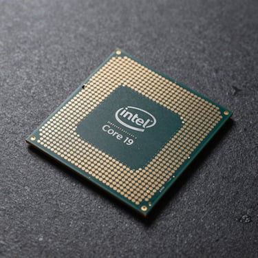 Overhead flat-lay of an Intel Core i9 processor on a neutral dark slate surface, studio strobe lighting, pin grid array underside visible at slight angle, sharp detail