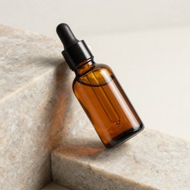 Amber glass dropper bottle resting on a block of light-colored marble, soft shadows.