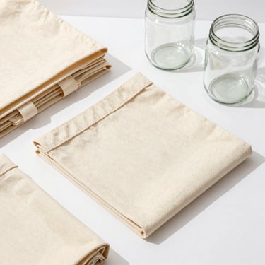 Flat-lay of heavy canvas storage bags and thick glass utility jars on a clean white surface with sharp shadows.
