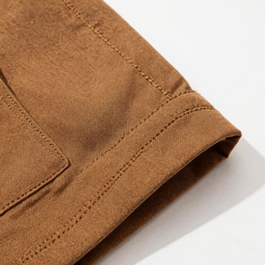 Close-up of a folded heavy-duty brown canvas work jacket showing reinforced triple-stitching details under bright natural light.