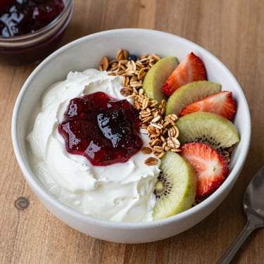 A happy woman enjoying a creamy yogurt in a bright kitchen.